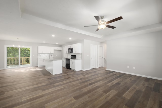 unfurnished living room with a tray ceiling, sink, dark wood-type flooring, and ceiling fan with notable chandelier