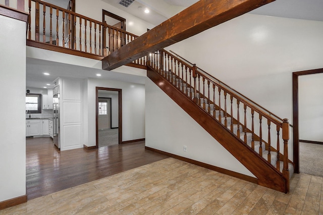 stairs with recessed lighting, wood finished floors, a towering ceiling, baseboards, and beam ceiling