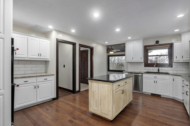 kitchen with a kitchen island, dark stone countertops, dark wood-type flooring, stainless steel dishwasher, and a sink