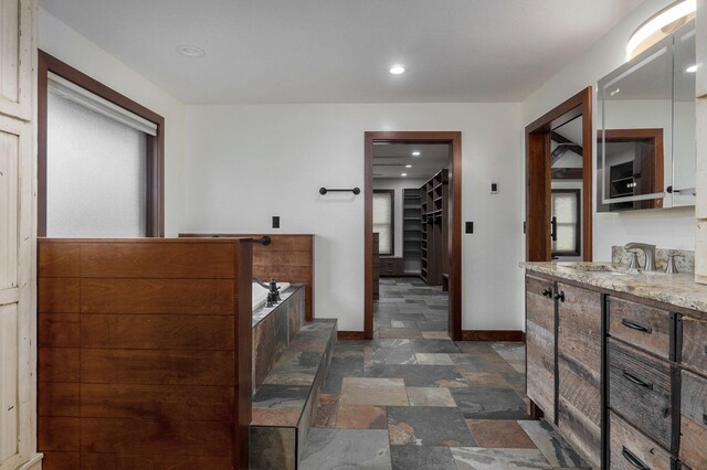 bathroom featuring a spacious closet, stone finish flooring, vanity, baseboards, and a bath