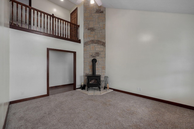 unfurnished living room featuring carpet floors, high vaulted ceiling, a wood stove, and baseboards