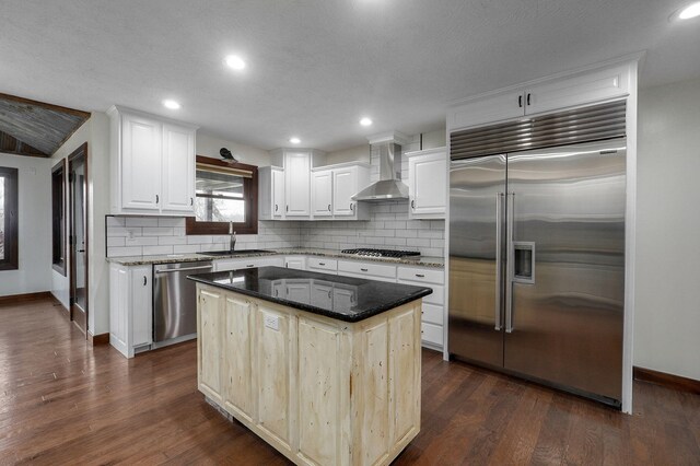 kitchen with stainless steel appliances, dark wood-style flooring, a sink, wall chimney exhaust hood, and tasteful backsplash