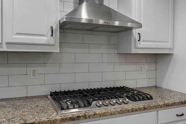 kitchen with light stone counters, under cabinet range hood, white cabinets, decorative backsplash, and stainless steel gas stovetop