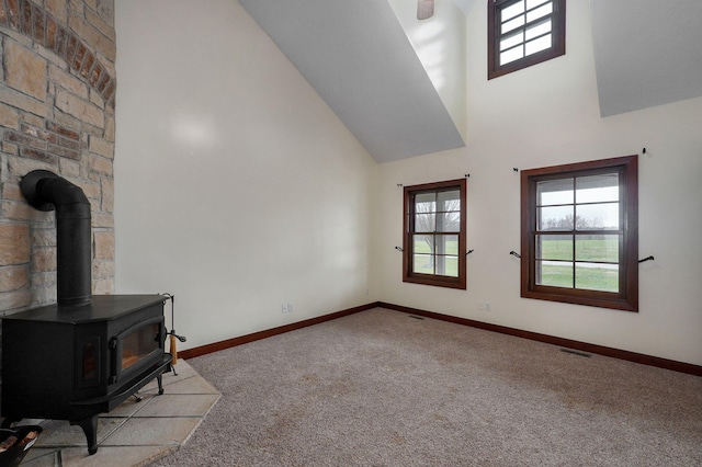 carpeted living area with visible vents, high vaulted ceiling, a wood stove, and baseboards