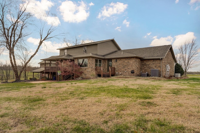 rear view of house with central AC unit, a lawn, a wooden deck, and brick siding