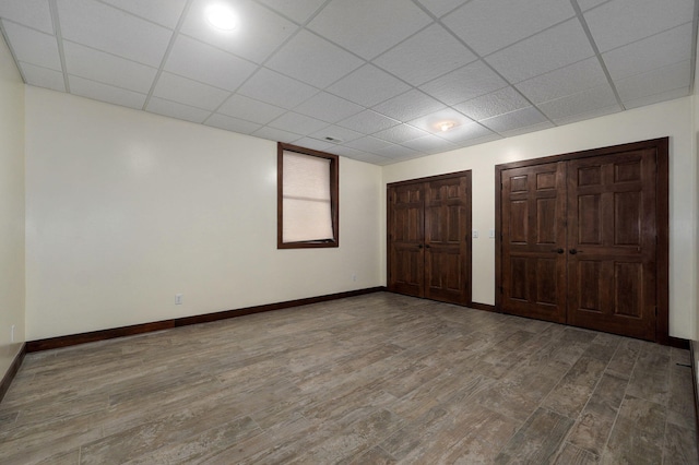 unfurnished bedroom featuring wood finished floors, a drop ceiling, two closets, and baseboards