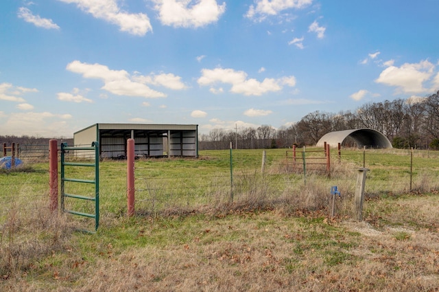 view of yard featuring a rural view, fence, a carport, and an outbuilding