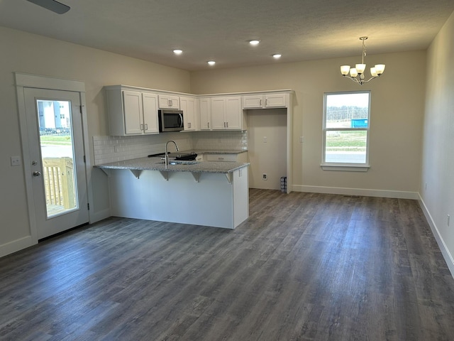 kitchen with white cabinets, decorative light fixtures, dark wood-type flooring, and a breakfast bar area