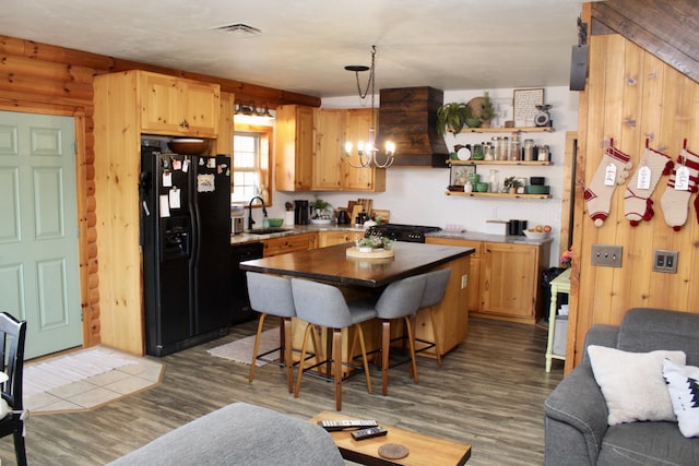 kitchen with black appliances, wood walls, custom range hood, and sink