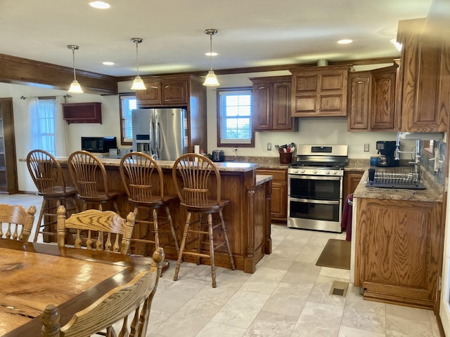 kitchen with stone countertops, a kitchen island, stainless steel appliances, and decorative light fixtures