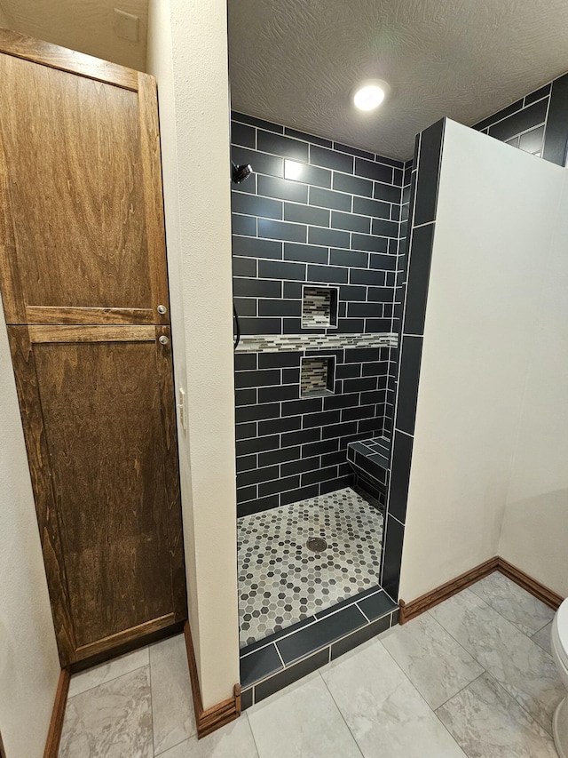 bathroom with a tile shower, a textured ceiling, and toilet