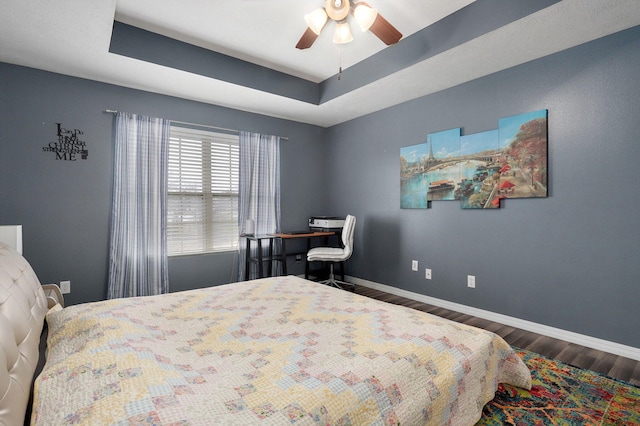 bedroom featuring ceiling fan, dark hardwood / wood-style flooring, and a tray ceiling