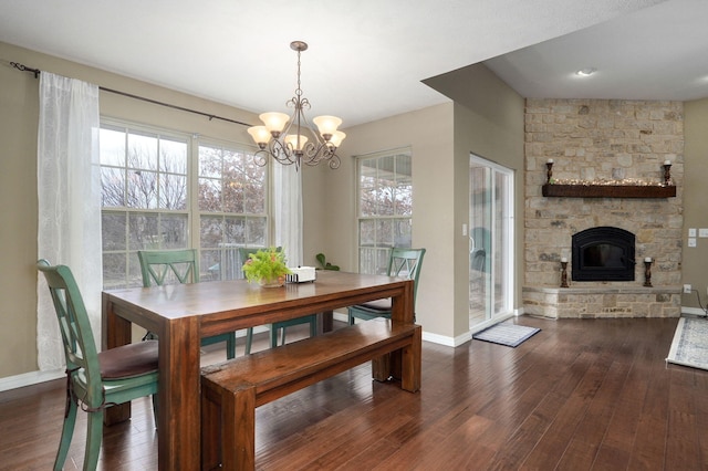 dining space with dark hardwood / wood-style flooring, an inviting chandelier, a stone fireplace, and a wealth of natural light