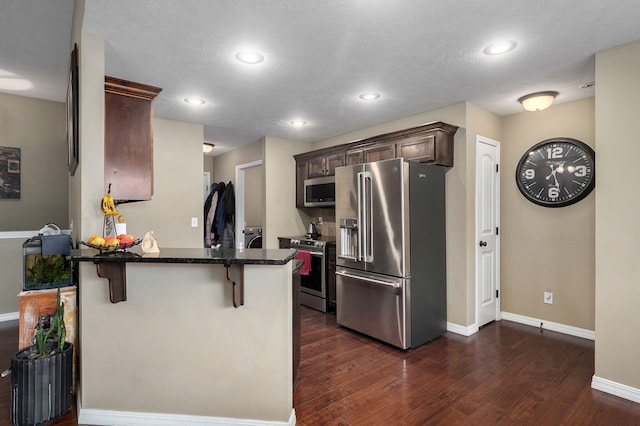 kitchen featuring kitchen peninsula, a breakfast bar area, dark hardwood / wood-style flooring, dark brown cabinetry, and stainless steel appliances