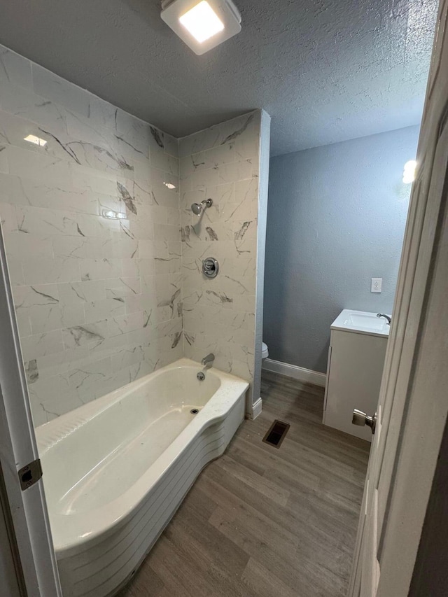 full bathroom with hardwood / wood-style floors, vanity, tiled shower / bath combo, toilet, and a textured ceiling