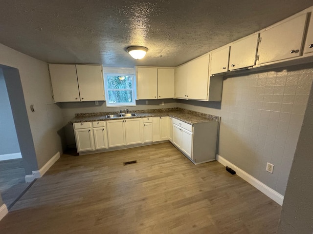 kitchen with a textured ceiling, light hardwood / wood-style flooring, white cabinetry, and sink