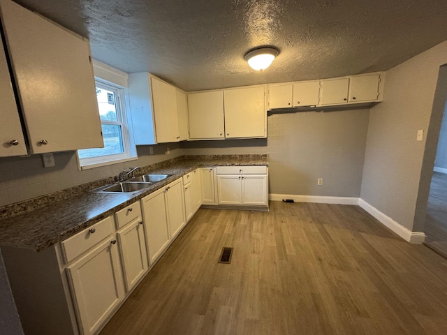 kitchen featuring white cabinetry, sink, tasteful backsplash, a textured ceiling, and light wood-type flooring