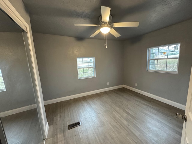 unfurnished bedroom with ceiling fan, wood-type flooring, and multiple windows