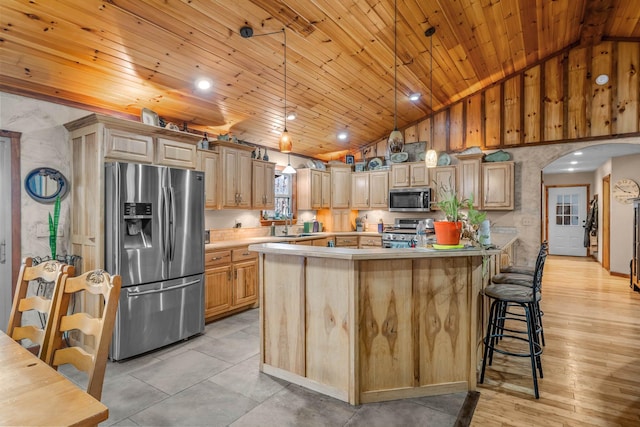 kitchen with pendant lighting, light brown cabinets, stainless steel appliances, and vaulted ceiling