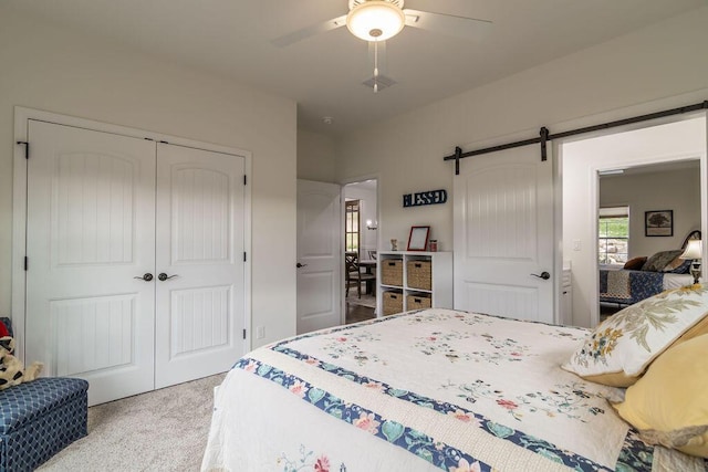 carpeted bedroom featuring a barn door, ceiling fan, and a closet