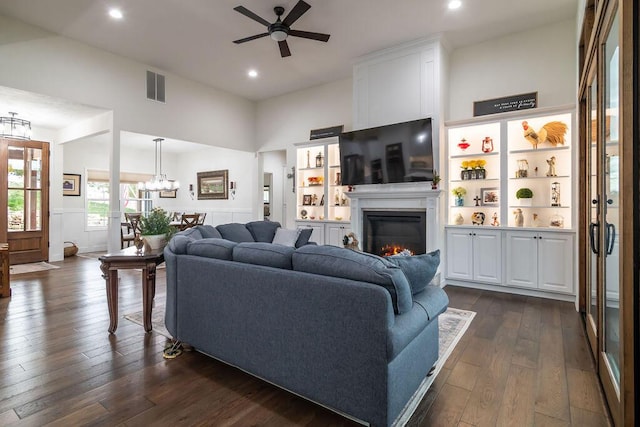 living room with a towering ceiling, dark wood-type flooring, and ceiling fan with notable chandelier