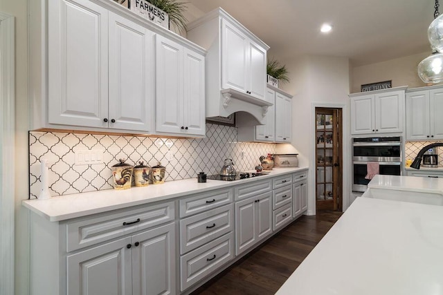 kitchen with black electric stovetop, white cabinets, stainless steel double oven, and dark hardwood / wood-style floors