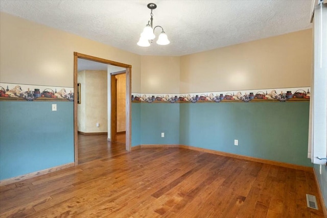 spare room featuring hardwood / wood-style floors, a textured ceiling, and an inviting chandelier