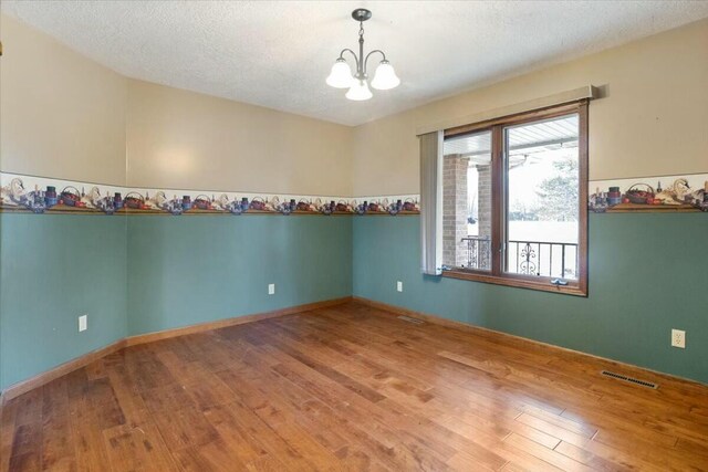 spare room featuring hardwood / wood-style floors, a textured ceiling, and a notable chandelier