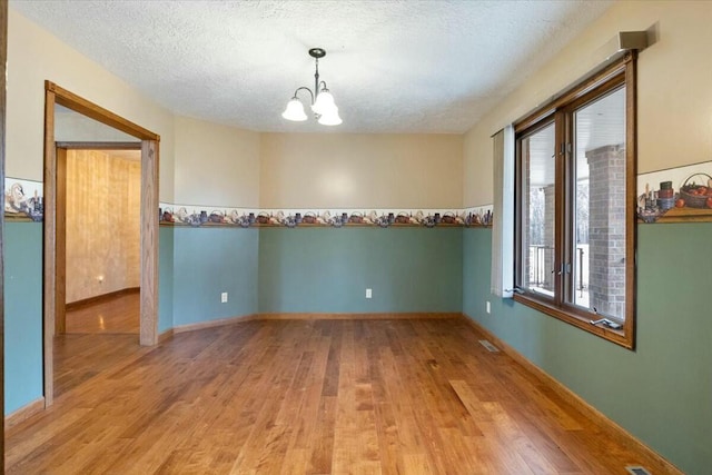 unfurnished room with a wealth of natural light, wood-type flooring, a textured ceiling, and a notable chandelier