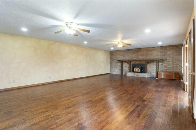 unfurnished living room with a textured ceiling, ceiling fan, dark hardwood / wood-style floors, and a brick fireplace