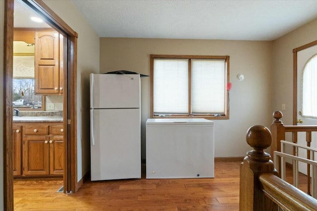 kitchen with light wood-type flooring, a textured ceiling, and white refrigerator