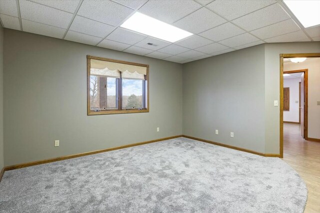 spare room with a paneled ceiling and light hardwood / wood-style flooring