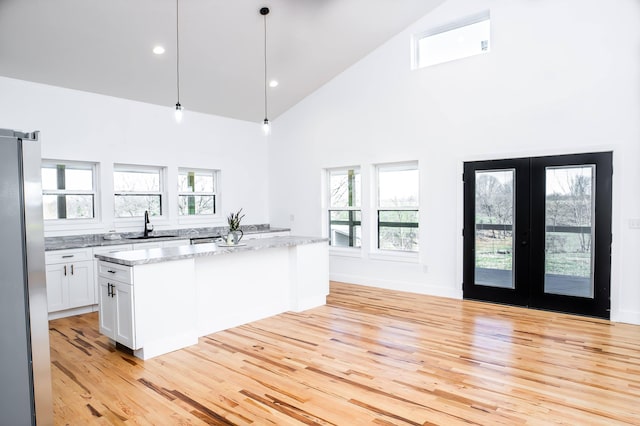 kitchen featuring high vaulted ceiling, hanging light fixtures, stainless steel fridge, light wood-type flooring, and white cabinetry