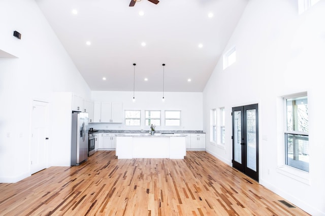 kitchen with a wealth of natural light, high vaulted ceiling, stainless steel appliances, and light hardwood / wood-style floors