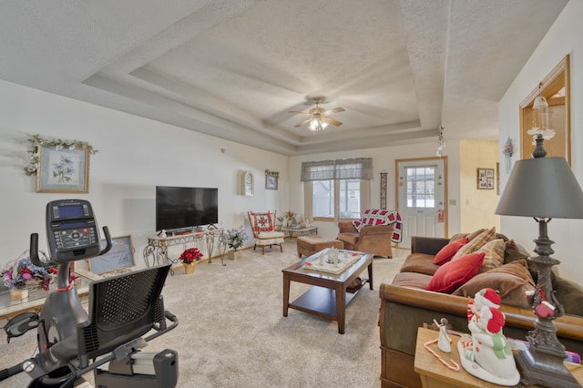 living room with a textured ceiling, light colored carpet, a raised ceiling, and ceiling fan