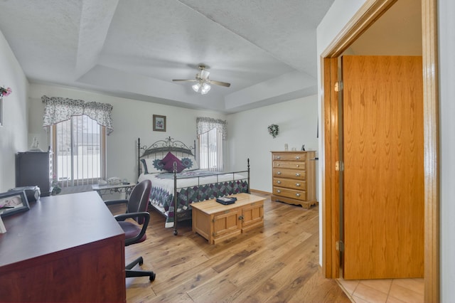 bedroom with a raised ceiling, light hardwood / wood-style flooring, and multiple windows