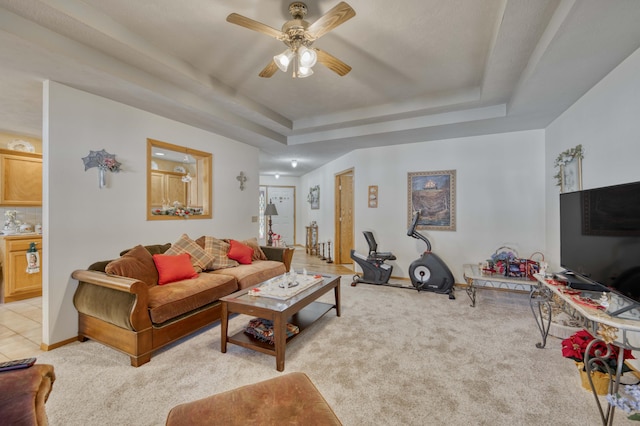 living room featuring light carpet, a tray ceiling, and ceiling fan