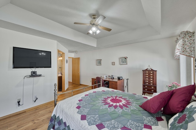 bedroom featuring hardwood / wood-style floors, ensuite bathroom, ceiling fan, and a tray ceiling