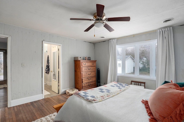 bedroom with ceiling fan, ensuite bathroom, wood walls, and light wood-type flooring