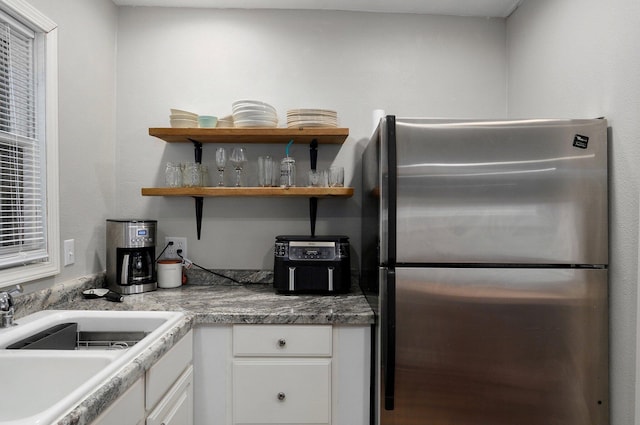 kitchen with stainless steel fridge, white cabinetry, and sink