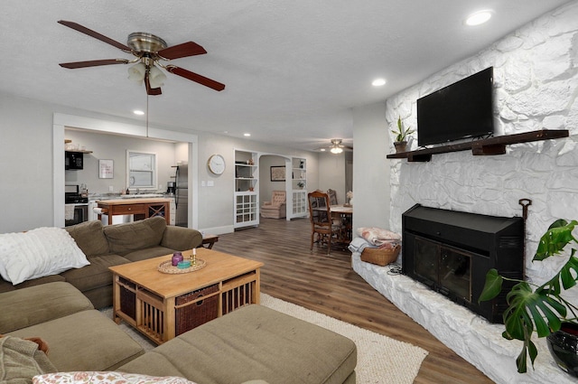 living room with a fireplace, a textured ceiling, dark hardwood / wood-style floors, and ceiling fan