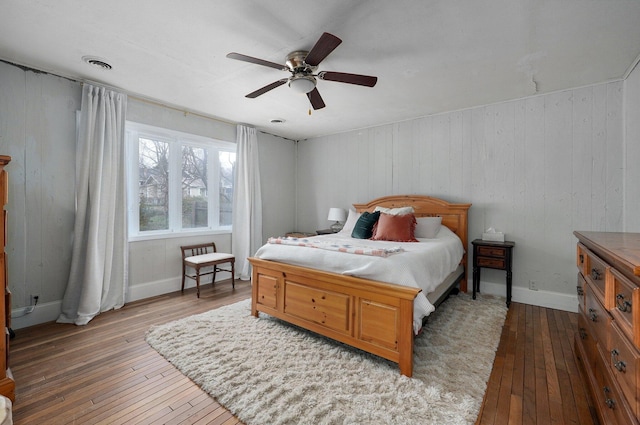 bedroom with hardwood / wood-style floors, ceiling fan, and wood walls