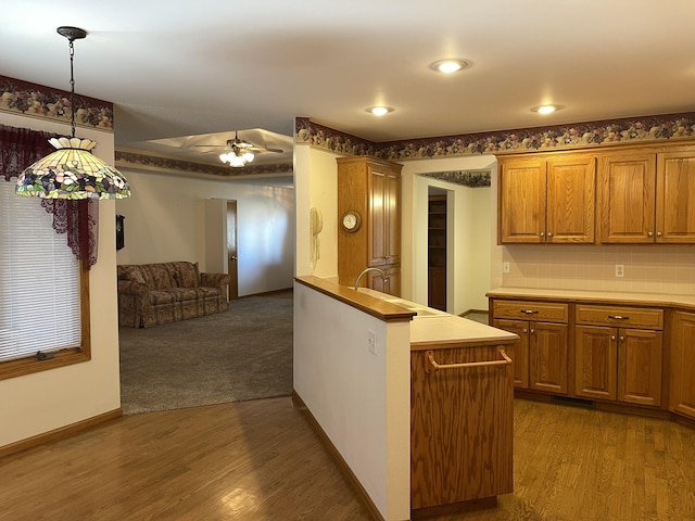 kitchen with ceiling fan, sink, backsplash, wood-type flooring, and decorative light fixtures