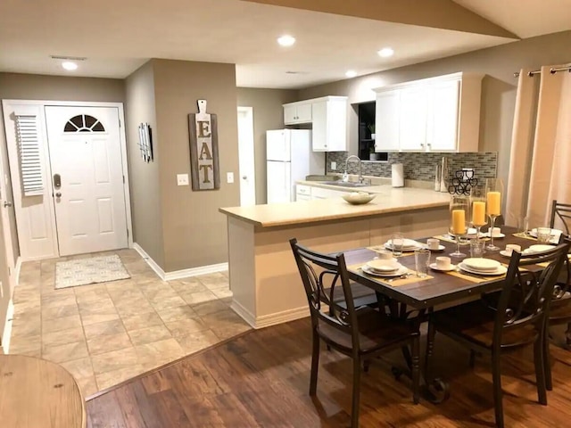 kitchen featuring white refrigerator, kitchen peninsula, decorative backsplash, white cabinets, and light wood-type flooring