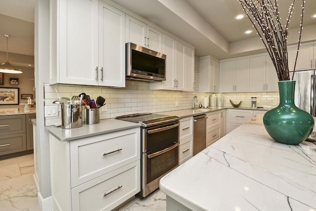 kitchen featuring decorative backsplash, appliances with stainless steel finishes, light stone counters, sink, and white cabinetry