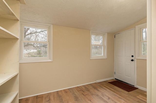 foyer featuring light wood-type flooring, a textured ceiling, and vaulted ceiling