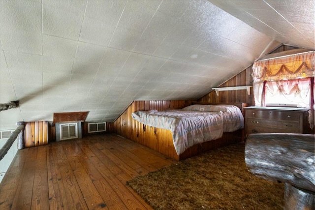 unfurnished bedroom with wooden walls, vaulted ceiling, and hardwood / wood-style flooring