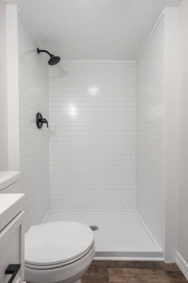 bathroom featuring a tile shower, toilet, vanity, and hardwood / wood-style flooring