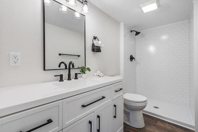 bathroom with hardwood / wood-style floors, vanity, a tile shower, and toilet