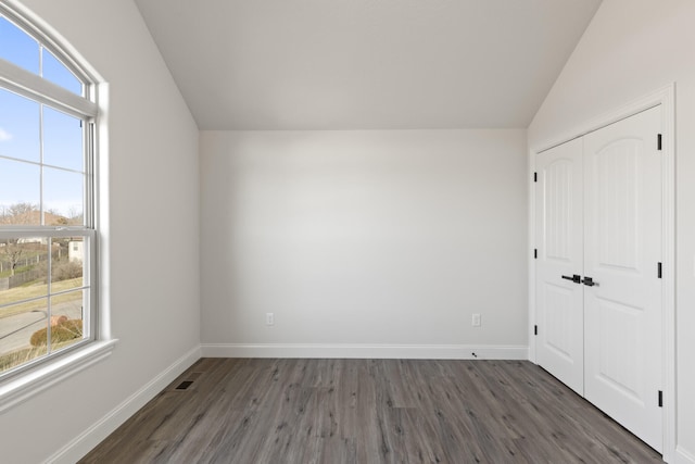 unfurnished bedroom with lofted ceiling, a closet, multiple windows, and dark wood-type flooring